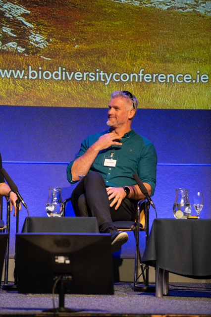 Speaker seated on a panel at a conference.